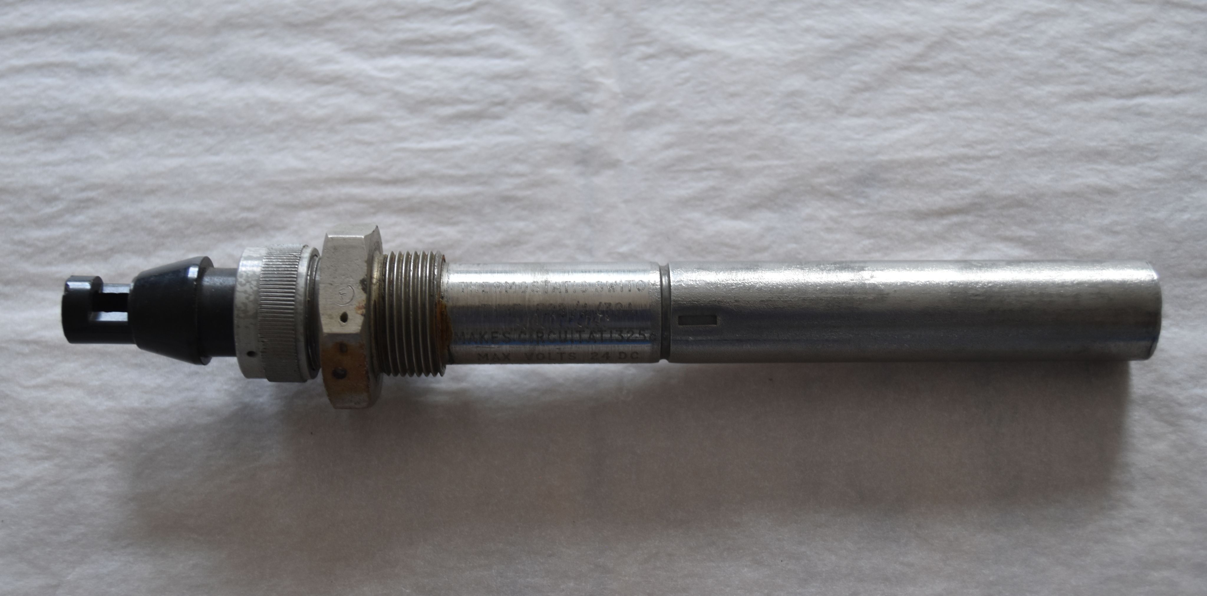 A thermostatic switch, a cylindrical metal object with screw elements and switch at left end.