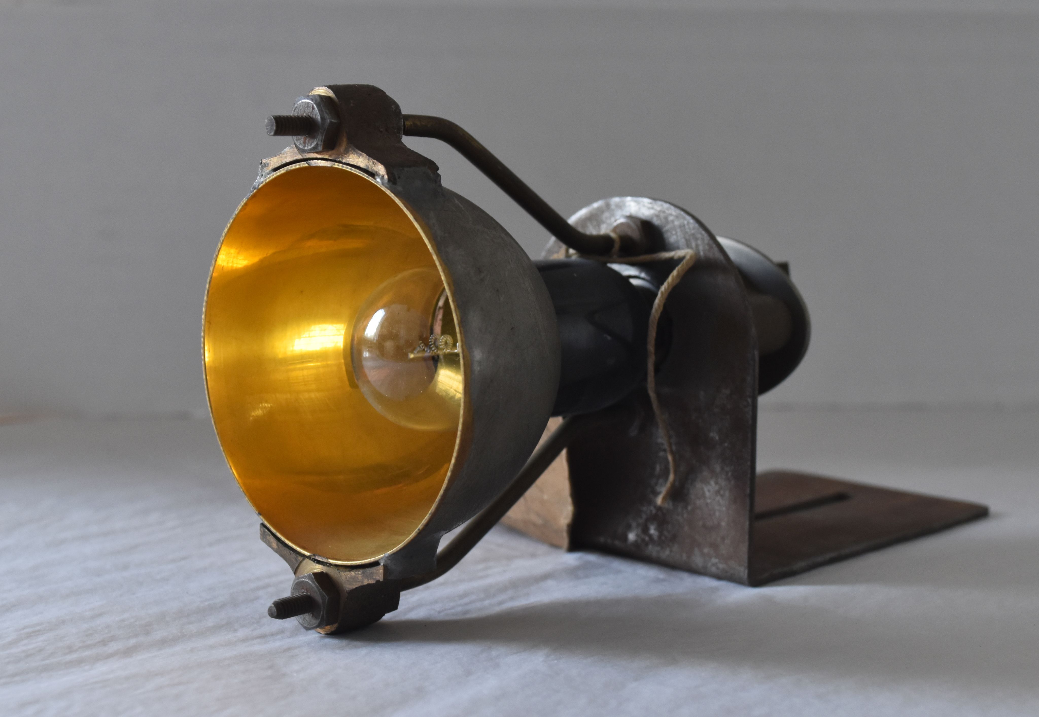 A small lamp on a bracket. Centre of lamp is gold in colour with a lightbulb present.