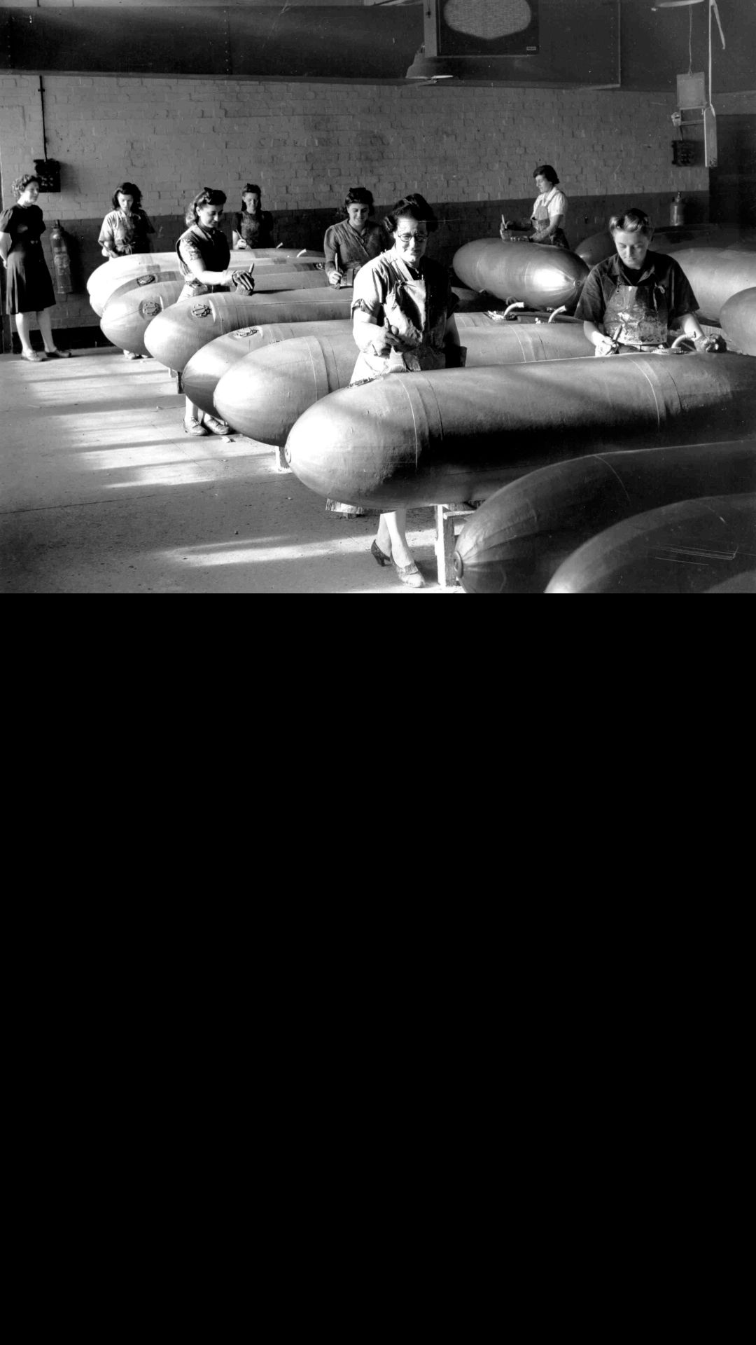 A black and white photograph of women in a factory making long range fuel drop tanks.
