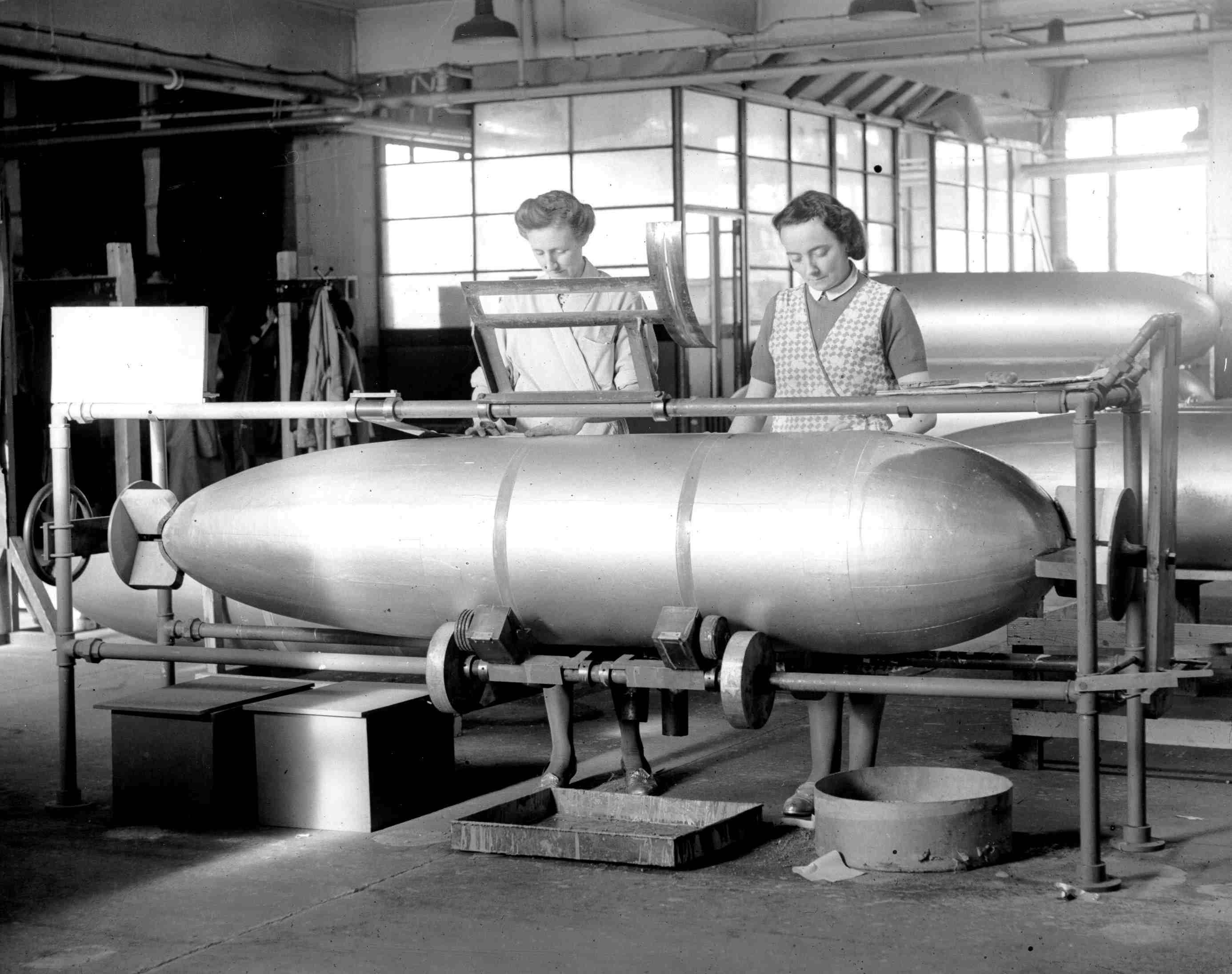 A black and white photograph of two women working with a large fuel drop tank.