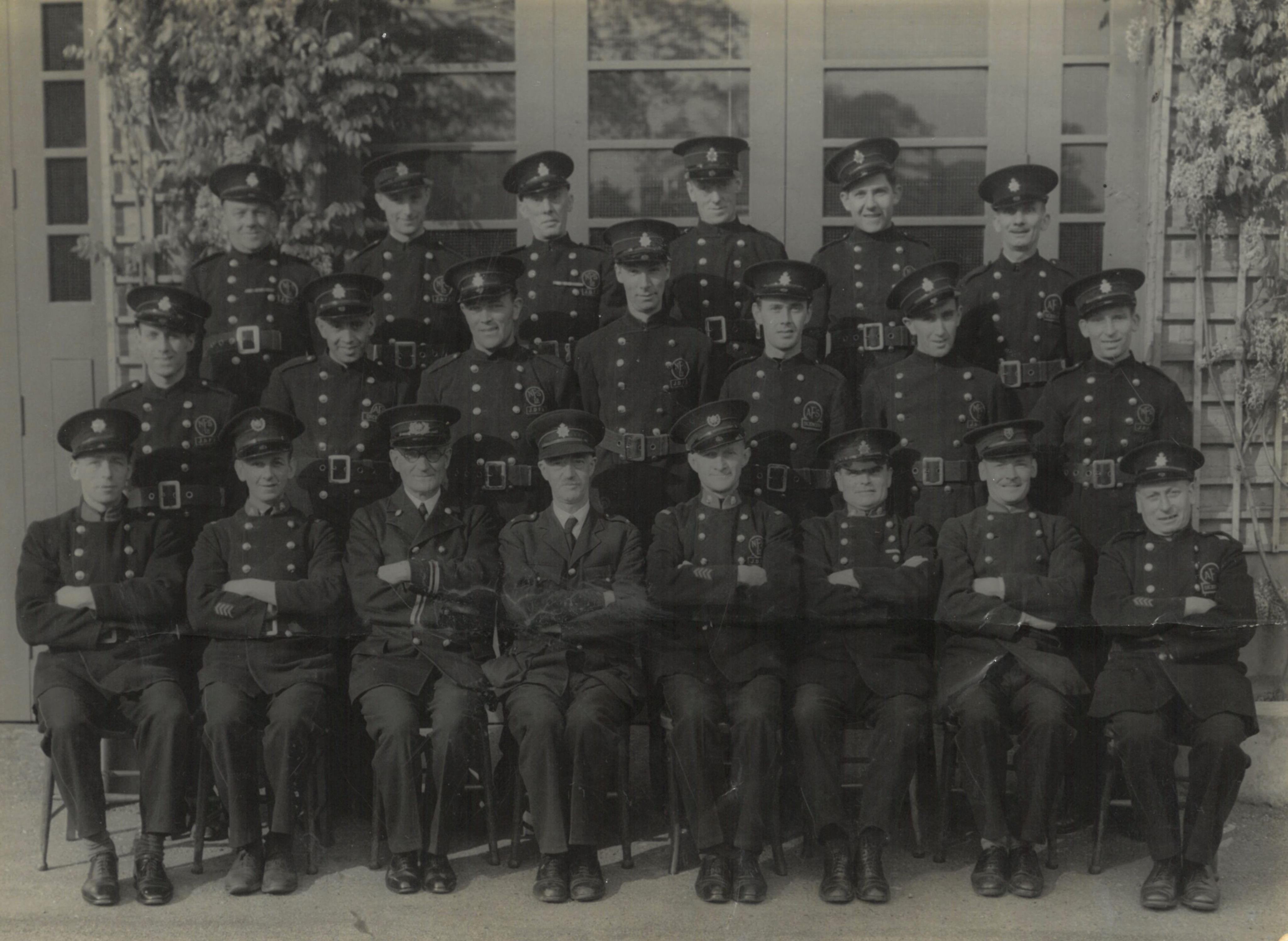 A black and white photograph of three rows of men dressed in formal fire brigade uniforms.